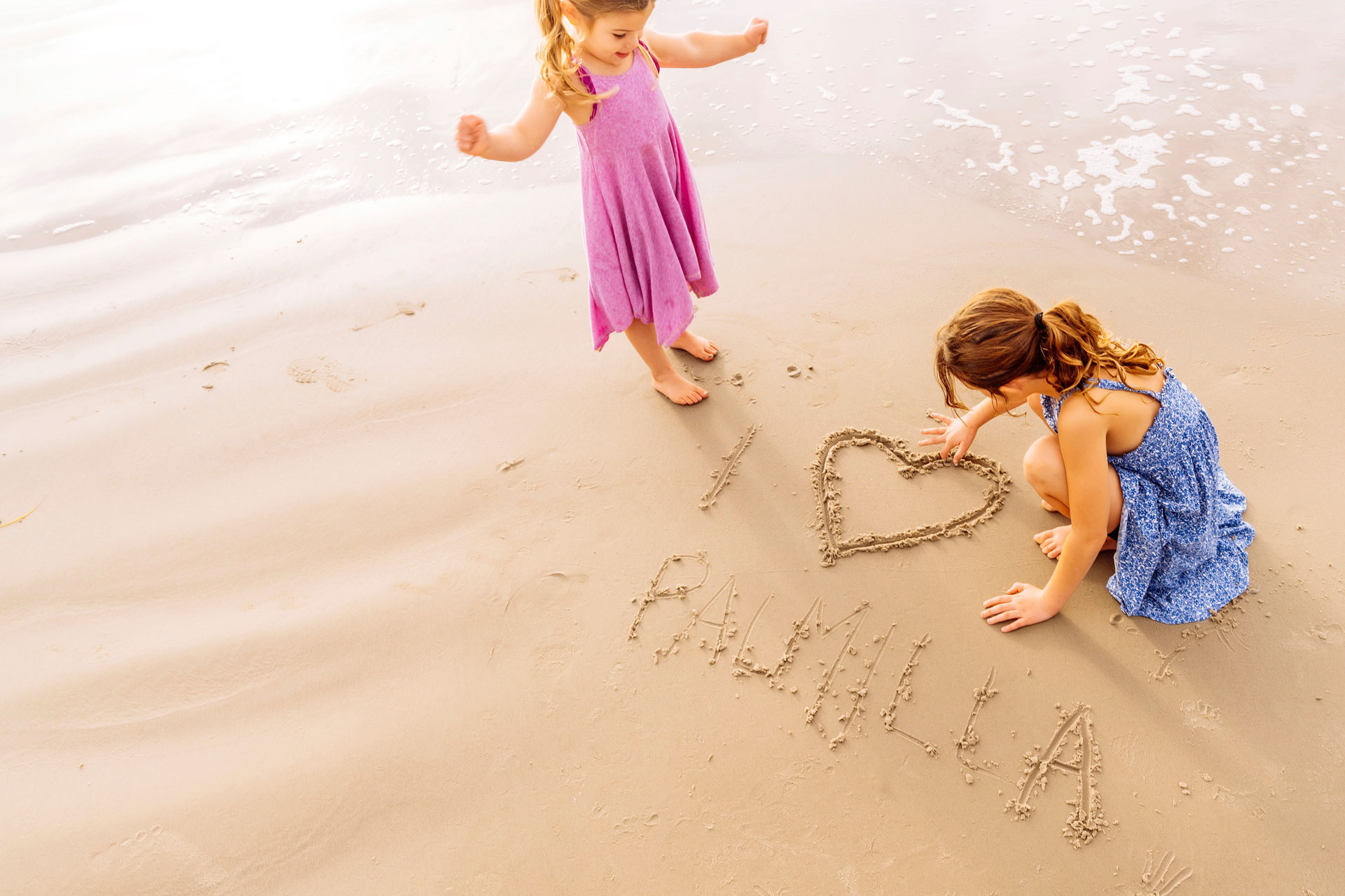 Two girls drawing a heart and writing “Palmilla” in the sand on Palmilla Beach