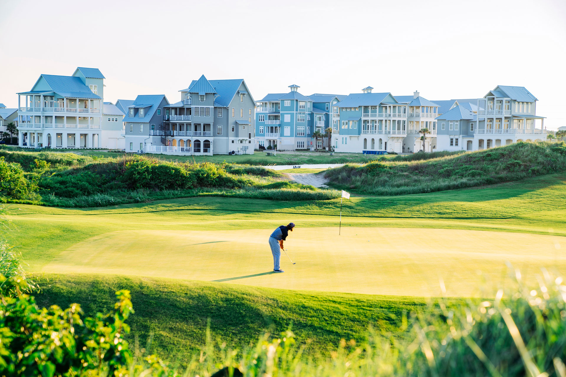 Golfer putting on a green with beach homes behind at Palmilla Beach