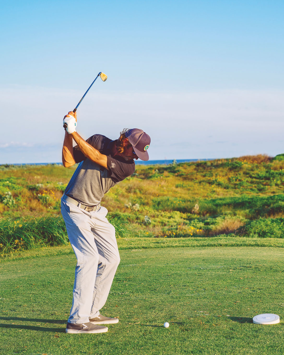 Golfer mid-swing on a tee box beside coastal dunes