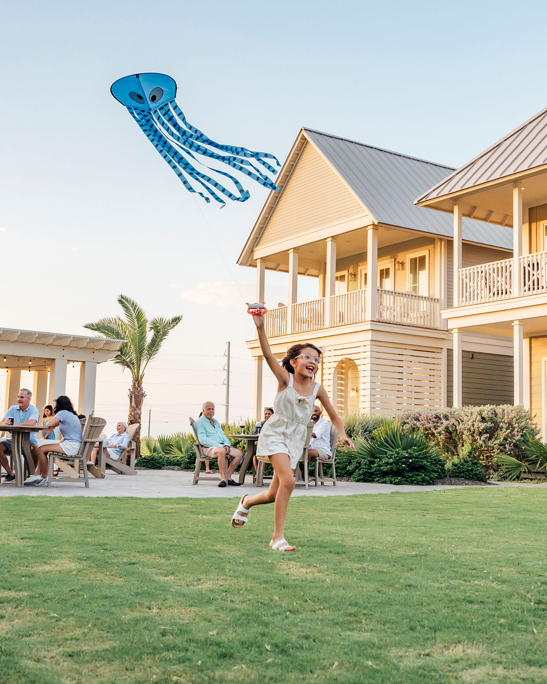 Girl flying an octopus kite on the lawn beside a beach house