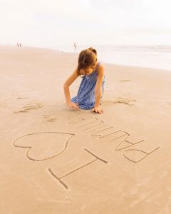 Girl writing "I love Palmilla" in the sand on the beach