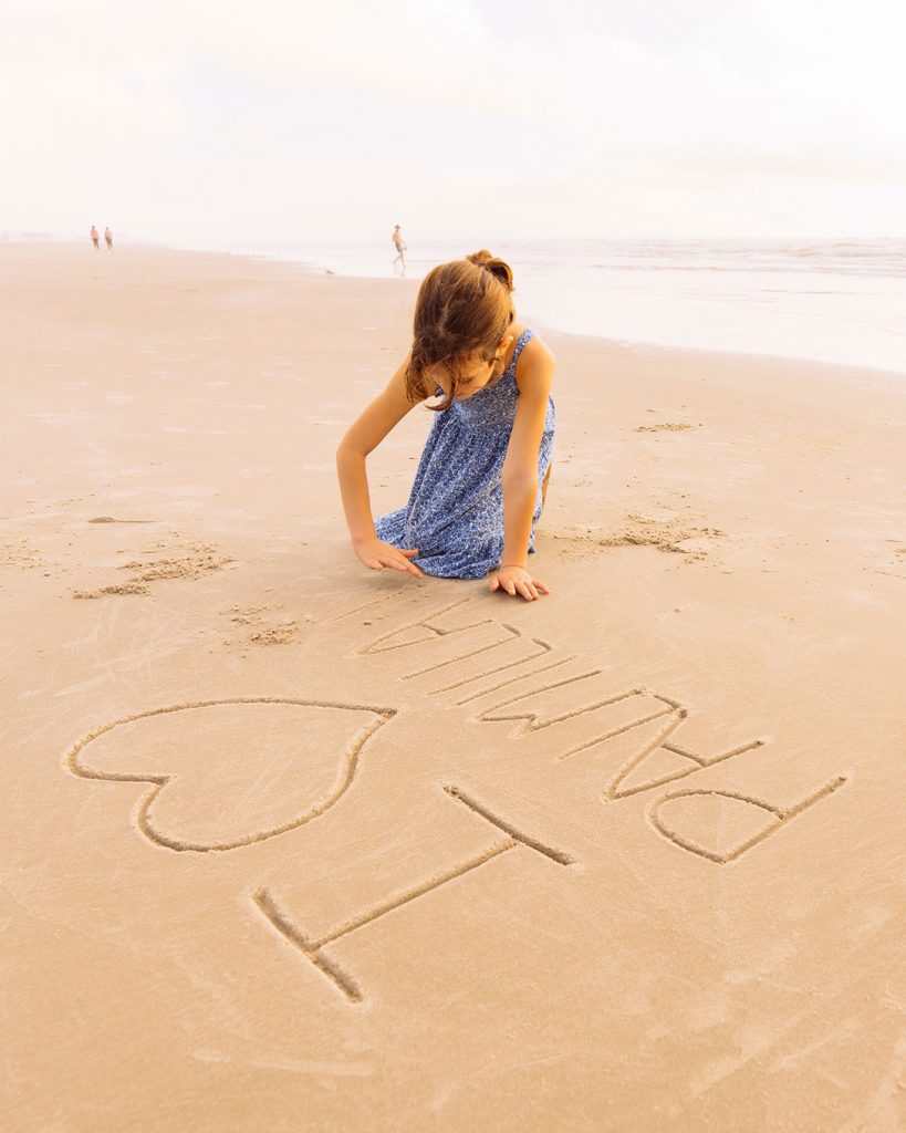 Girl writing "I love Palmilla" in the sand on the beach