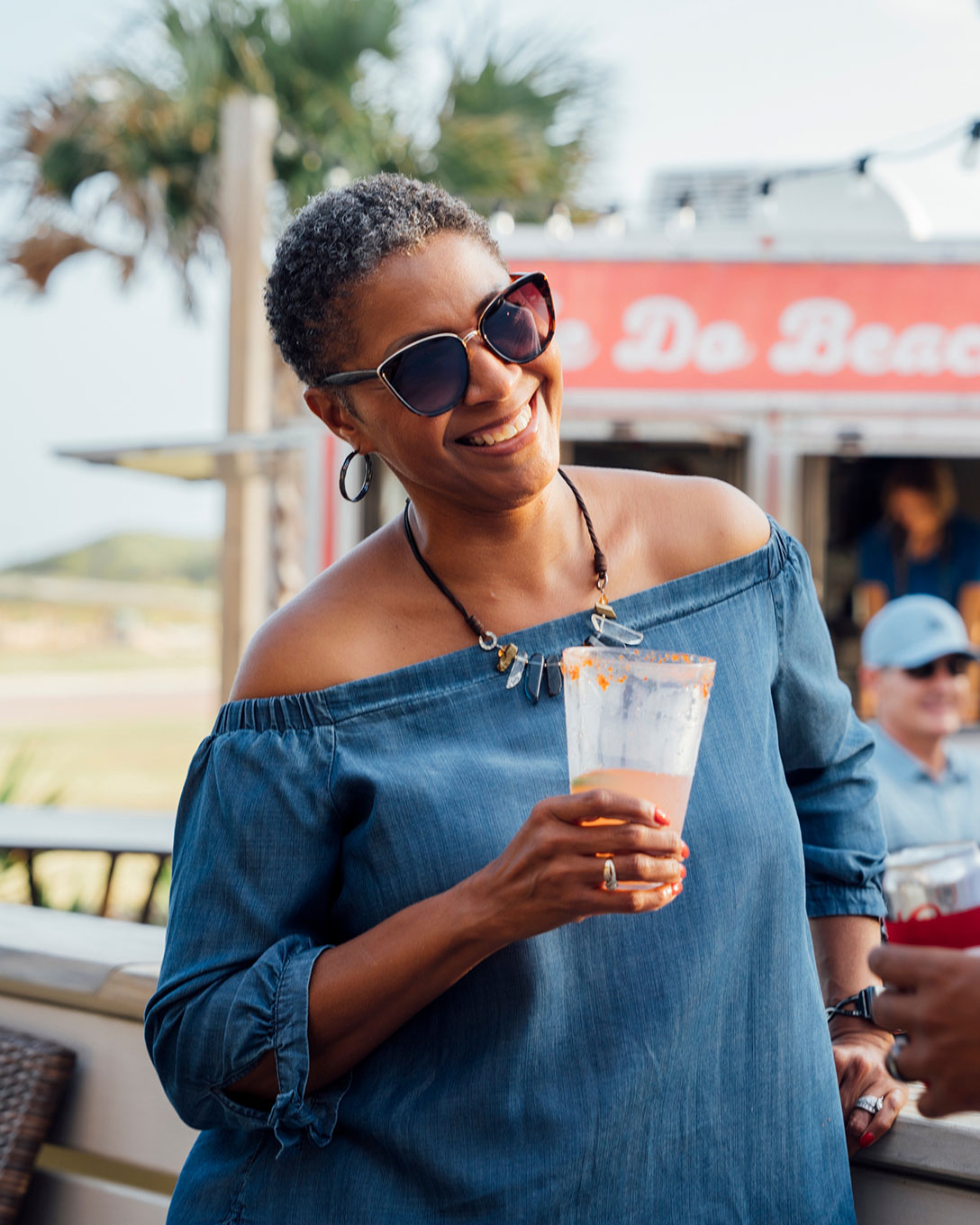 Smiling woman in sunglasses enjoying a drink at an outdoor bar