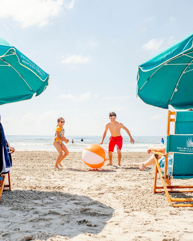 Kids playing with a beach ball between teal beach umbrellas