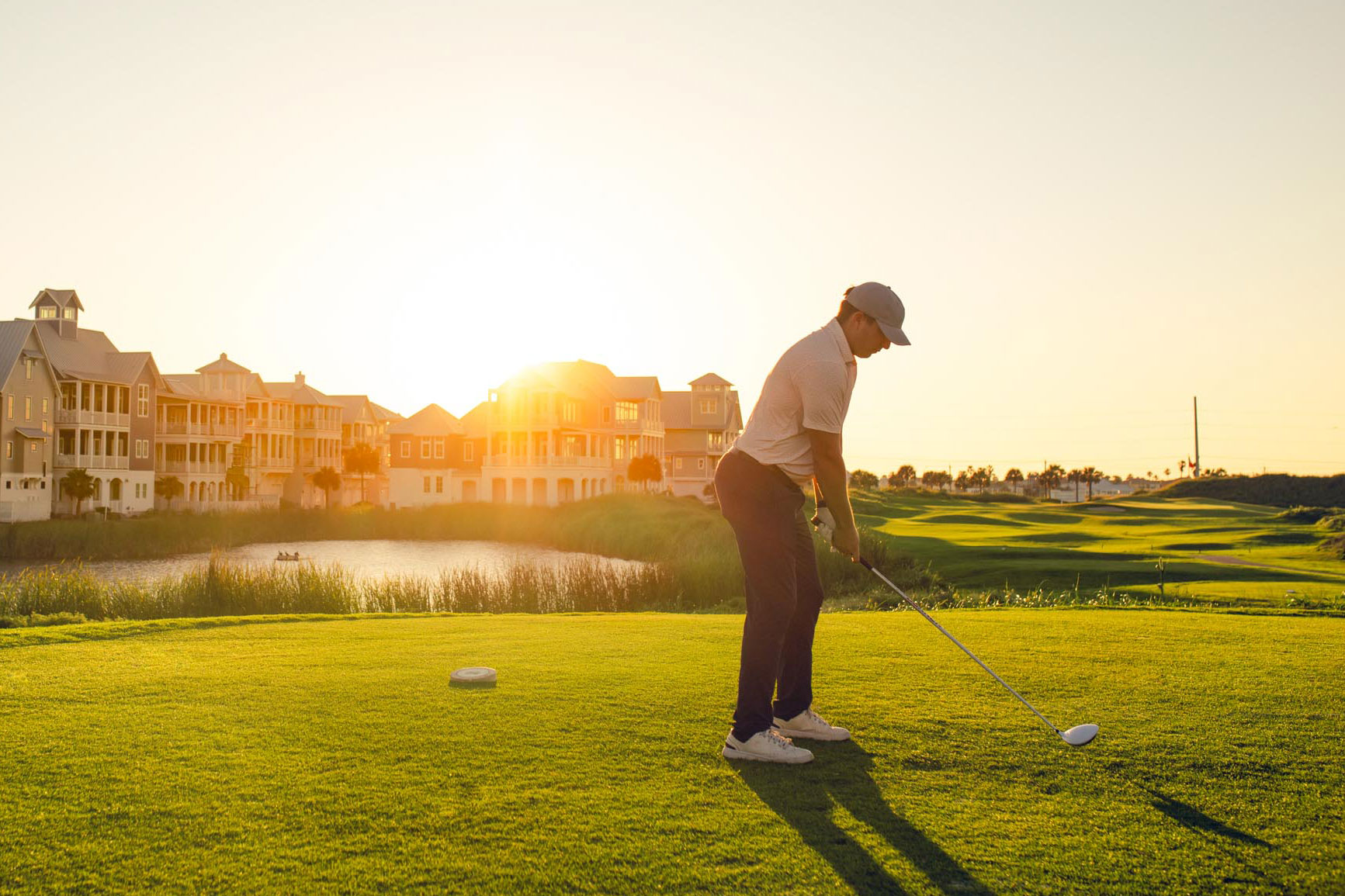 Golfer putting at sunset with resort buildings in the background