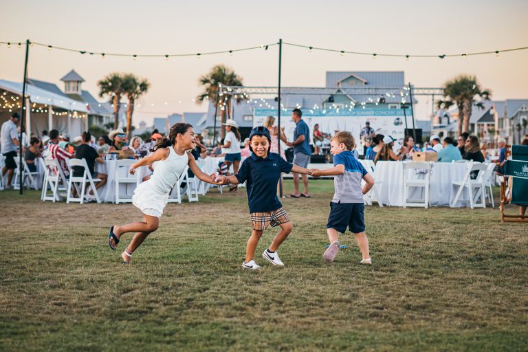 Families playing on the lawn under string lights at a Palmilla Beach community event