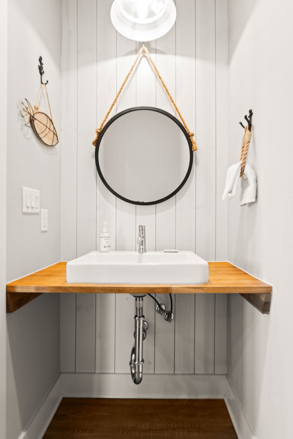 Powder room with a floating wood vanity and round mirror at 200 Sunset Avenue