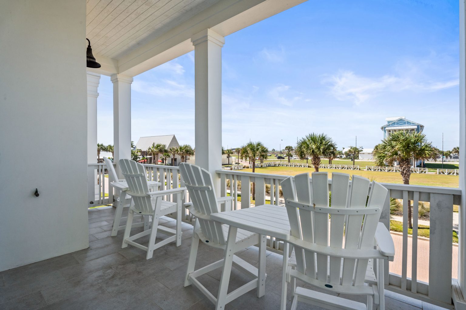 Covered porch with tall white dining chairs and palm views at 250 Sunrise Avenue