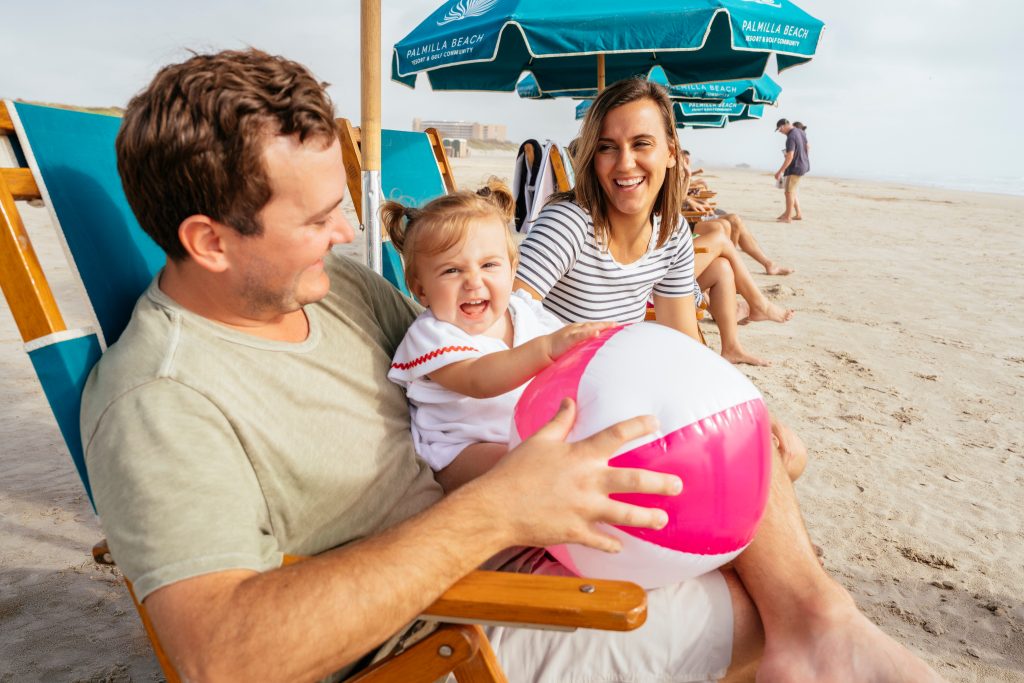 Family laughing with a beach ball under a Palmilla Beach umbrella