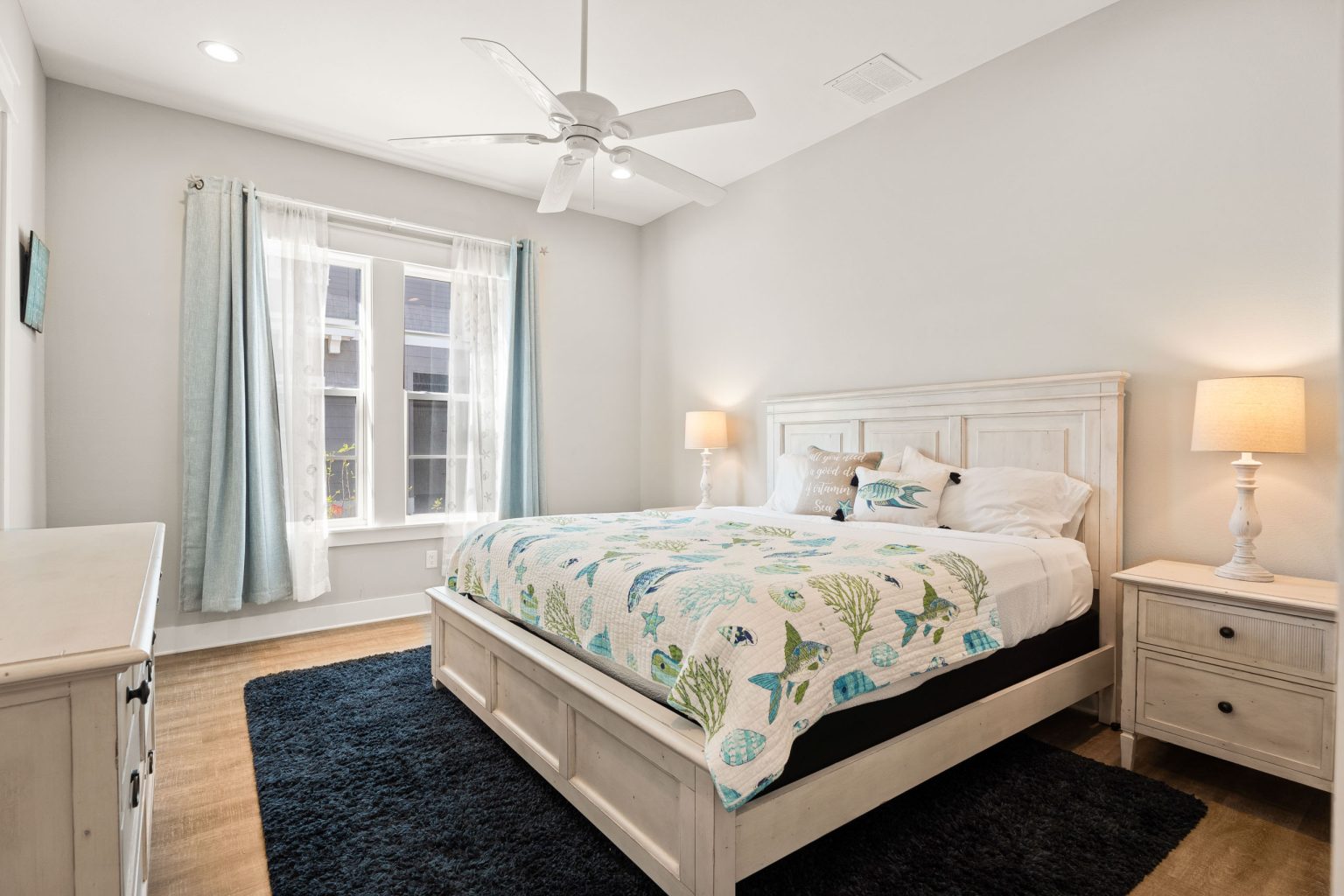 Bedroom with a white bed, ceiling fan and large windows at 200 Sunset Avenue