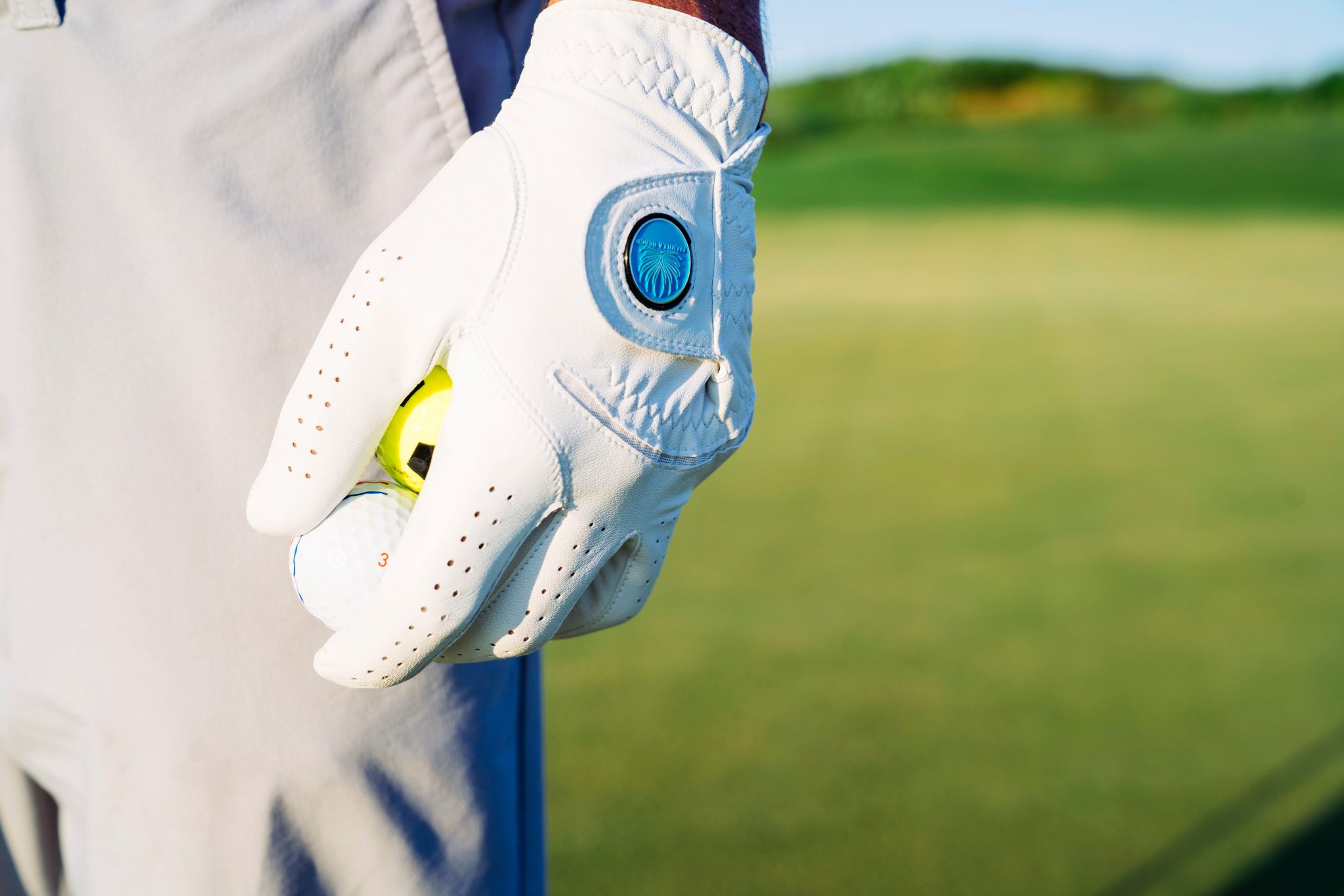 A golfer's gloved hand with a Palmilla Beach ball marker, holding golf balls