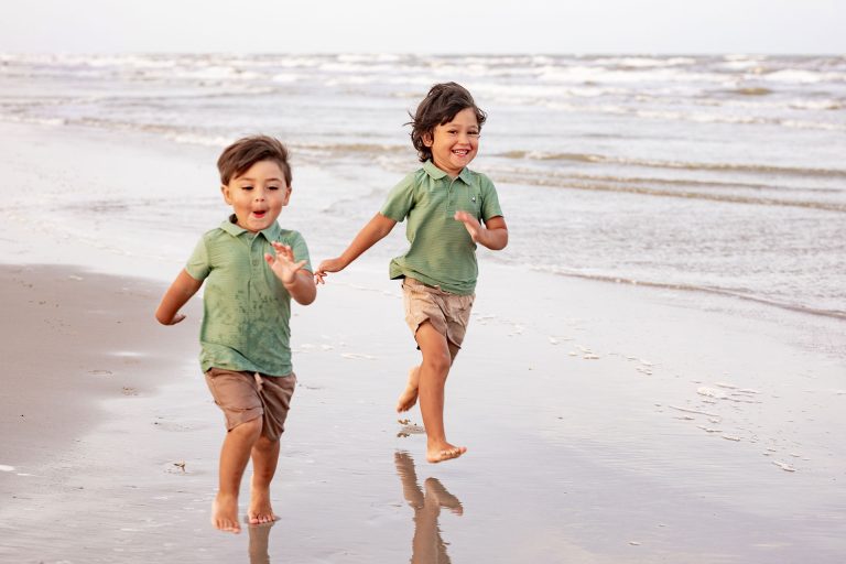 Two young boys running along the beach at the water's edge