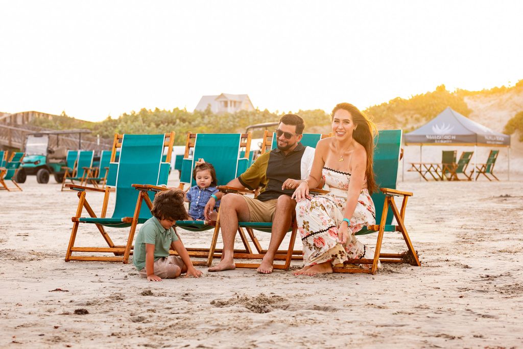 Family relaxing in teal beach chairs on the sand at sunset