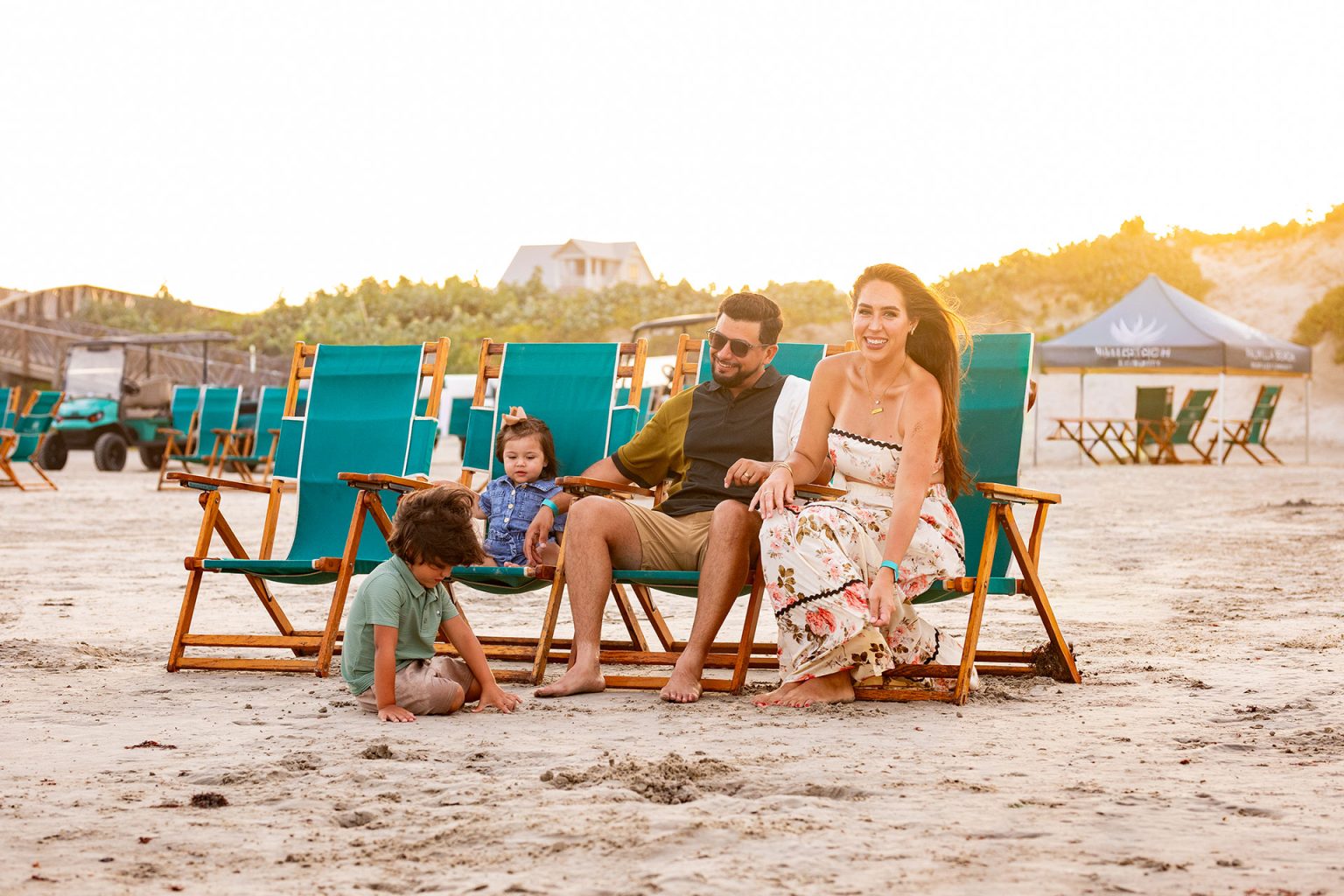 Family relaxing in teal beach chairs on the sand at sunset