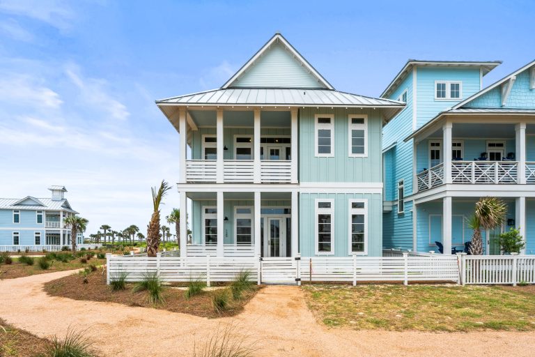 Front of 120 Lotus Lane, a two-story light blue home with double porches at Palmilla Beach