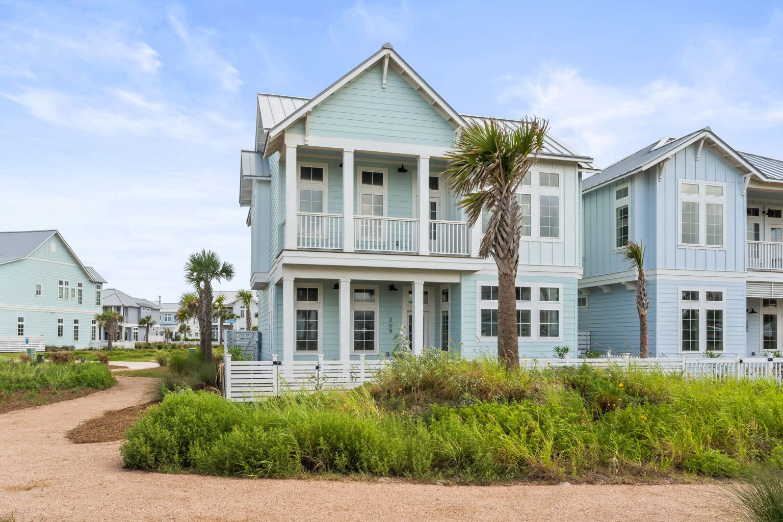 Front of 209 Horse Tail Lane, a light blue two-story home with palms at Palmilla Beach