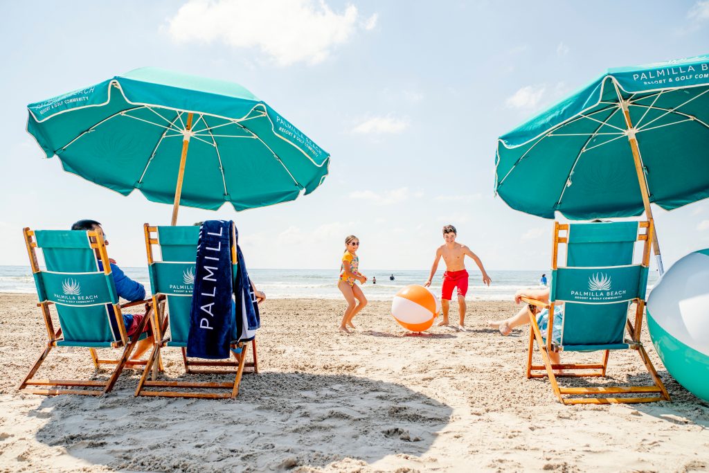 Families playing beach ball between Palmilla Beach umbrellas and loungers