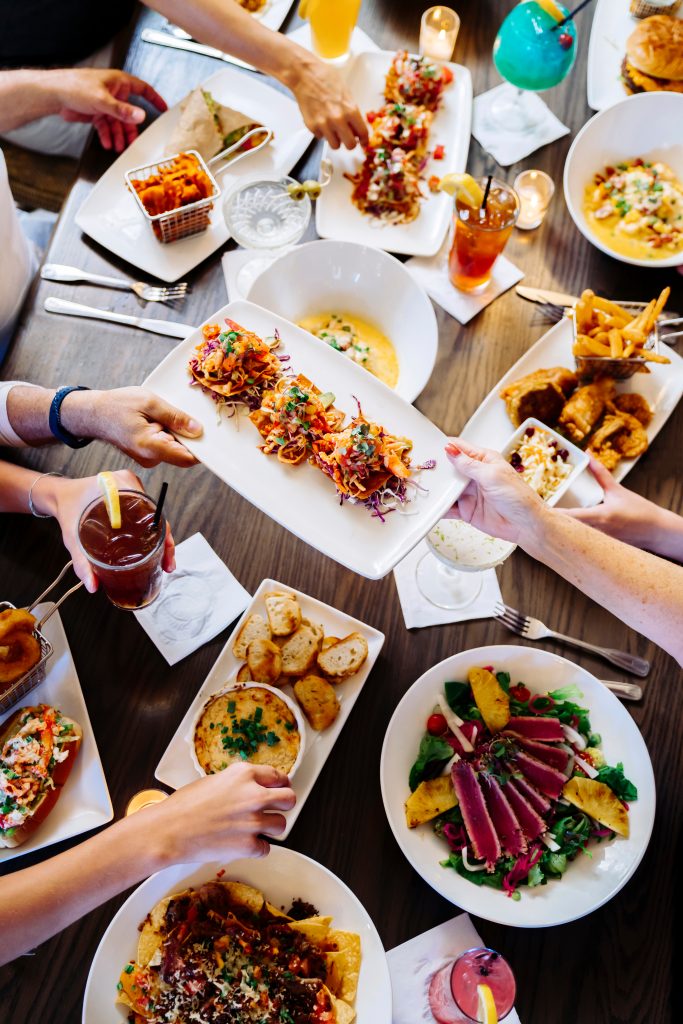 Friends sharing a table of coastal dishes and drinks at Palmilla Beach