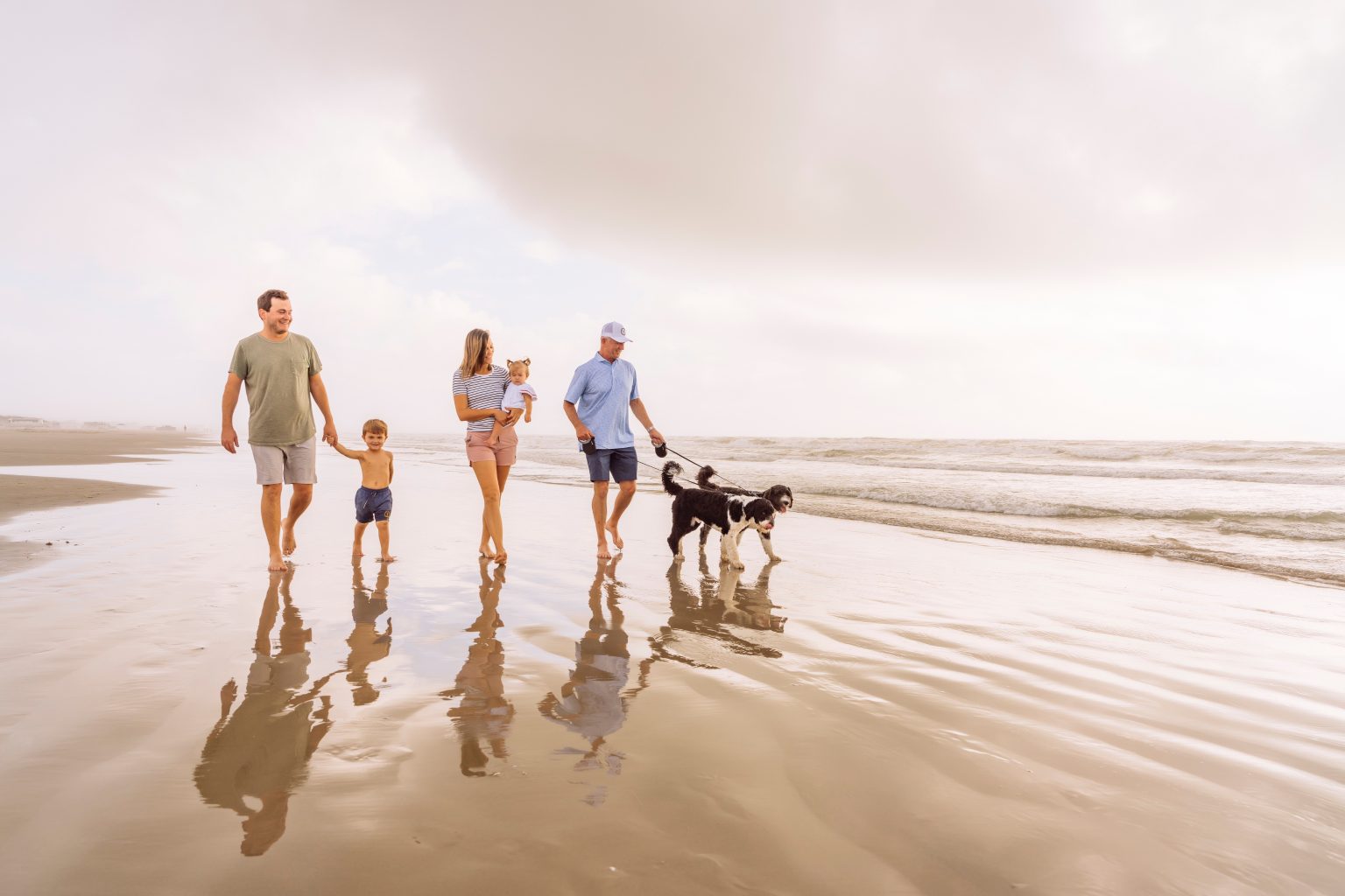 A family walking a dog along the water's edge on Palmilla Beach