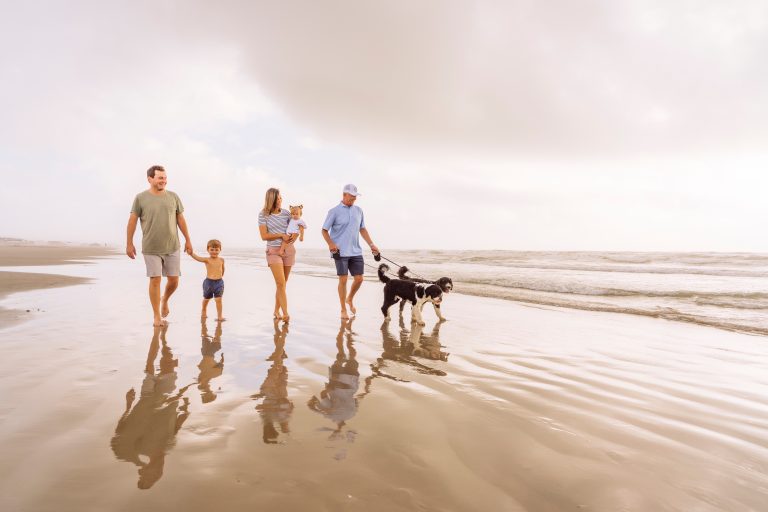 A family walking a dog along the water's edge on Palmilla Beach