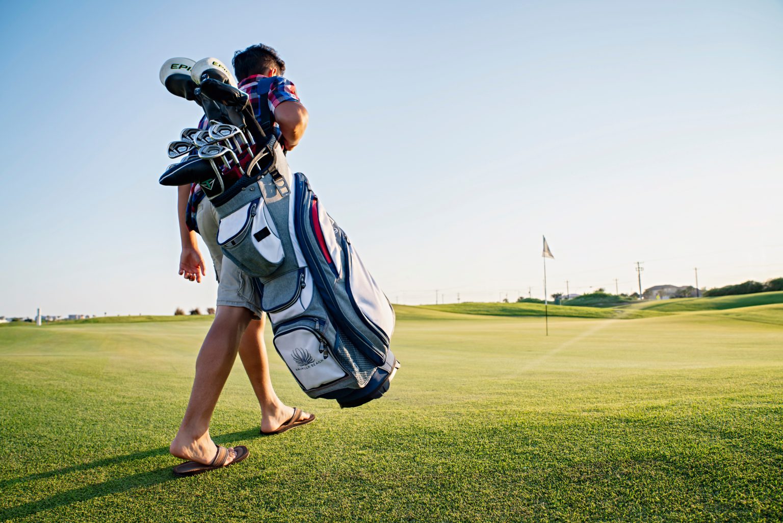 A golfer carrying a bag of clubs across the course on a bright day